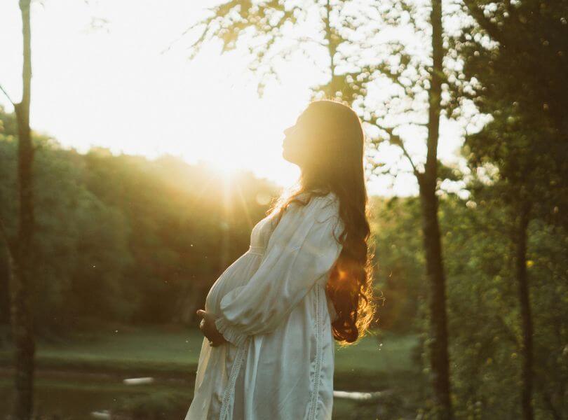 Femme enceinte dans un cadre naturel au coucher du soleil, symbolisant la préparation sereine à la conception.