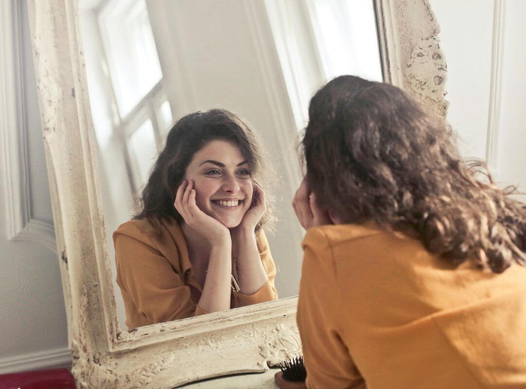 Femme souriante devant un miroir, reflétant l’espoir d’un quotidien sans douleur et en harmonie avec son corps.